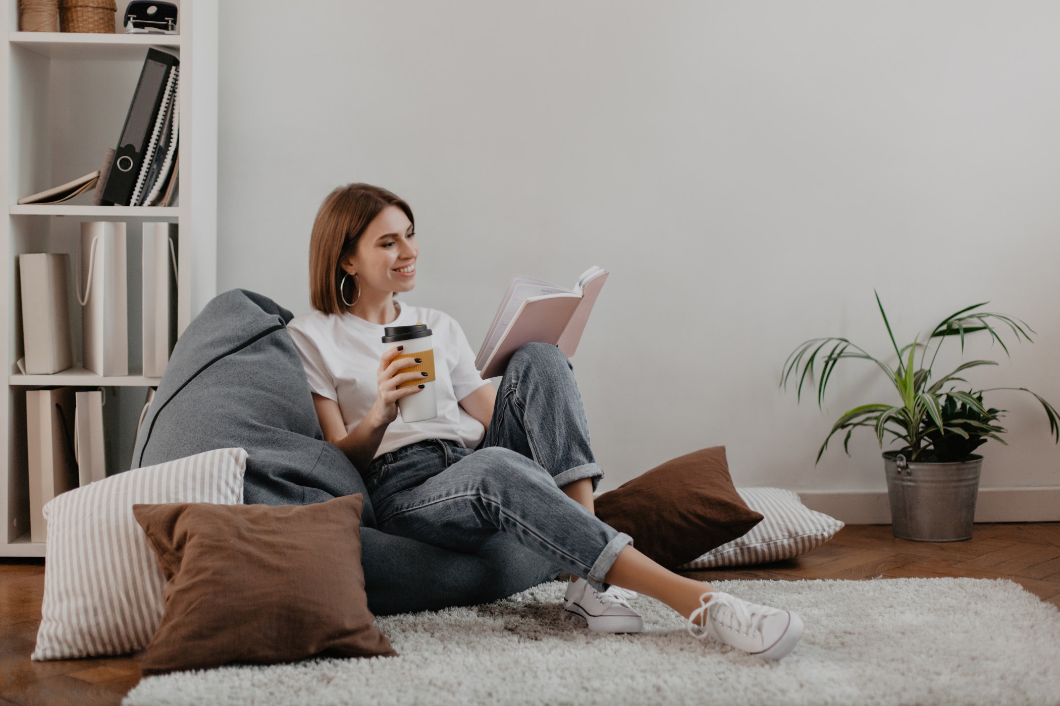 short haired girl in white t shirt with smile reading book while sitting on soft bean bag